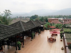 A covered outdoor area with wooden flooring, tables, chairs, and umbrellas.