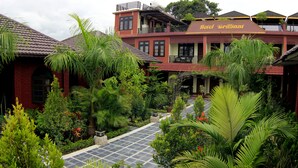 A hotel with a red facade, a balcony, and lush greenery.