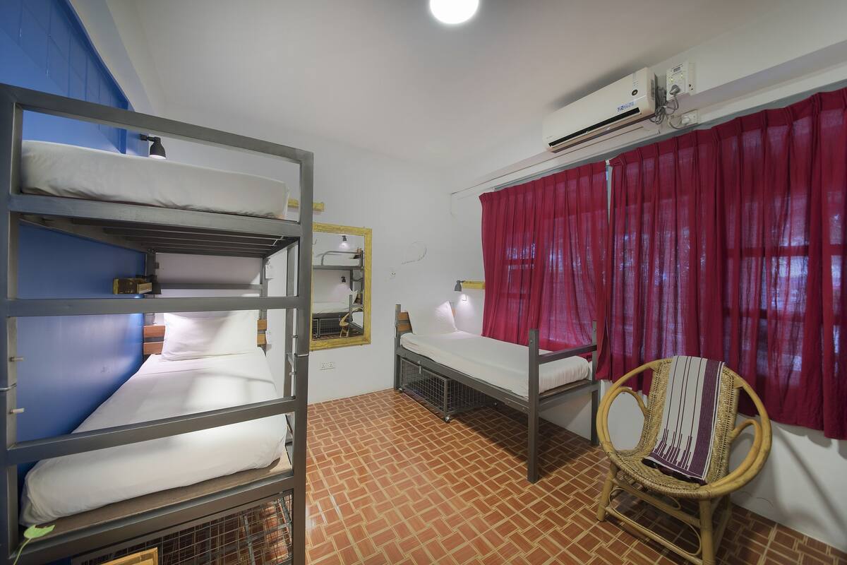 Une chambre de dortoir équipée de lits superposés, d’un lit simple, d’une chaise et d’un appareil de climatisation.