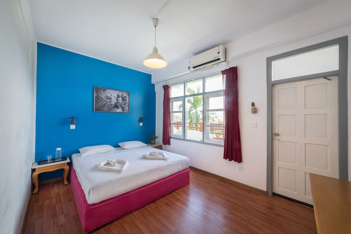 Une chambre à coucher comprenant un lit, une table de chevet, une fenêtre avec des rideaux, un appareil de climatisation et une porte.