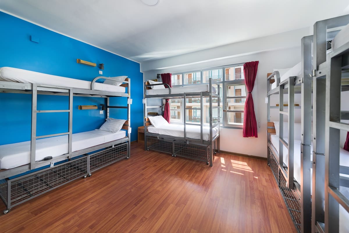 Une chambre de dortoir avec des lits superposés, une fenêtre avec des rideaux et un mur bleu.