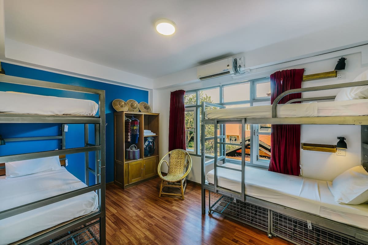 Une chambre de dortoir avec des lits superposés, un plancher en bois, une chaise, une armoire et une fenêtre donnant sur un paysage agréable.