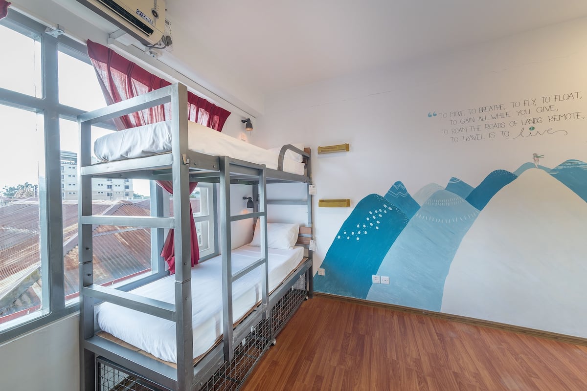Une chambre avec des lits superposés, un mur décoré d’une fresque et une fenêtre donnant sur une voie ferrée.