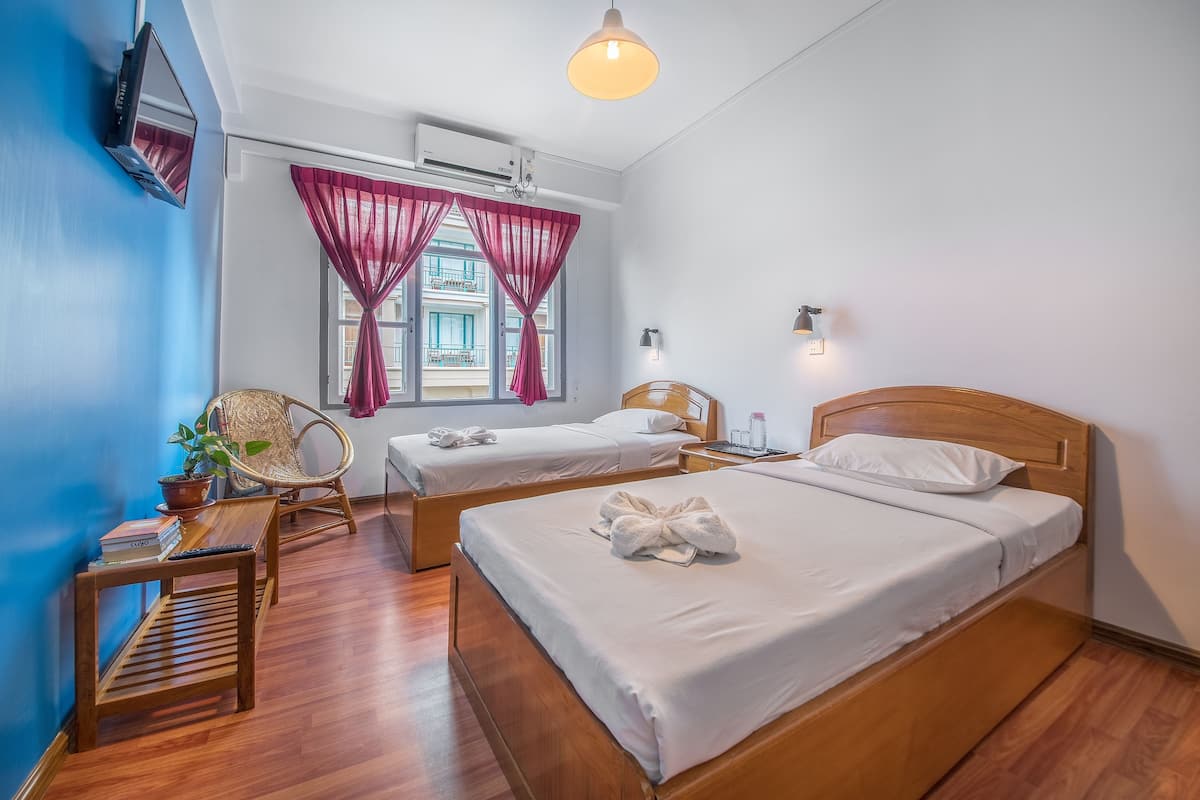 Une chambre d’hôtel avec deux lits, un plancher en bois, un téléviseur fixé au mur et une fenêtre avec des rideaux rouges.