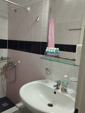 A bathroom with a shower, sink, and glass shelf with toiletries.