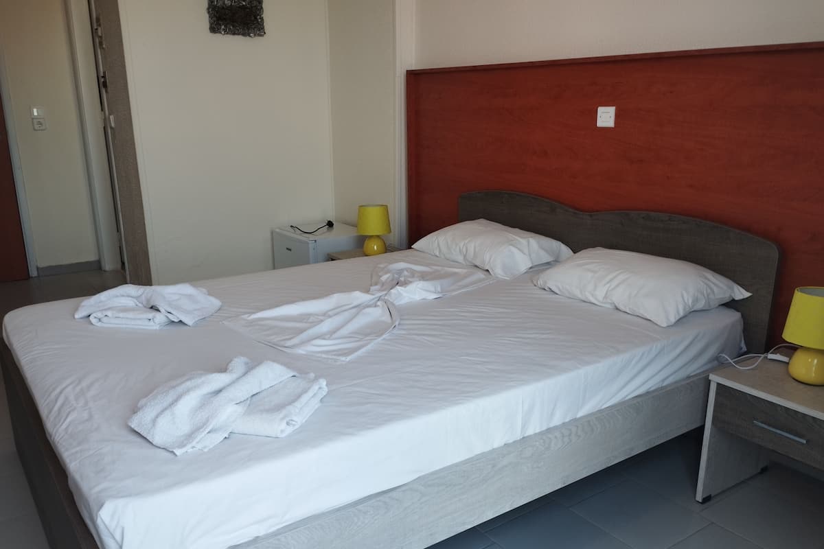 A hotel room with a large bed, a bedside table with a lamp, and a small cabinet.
