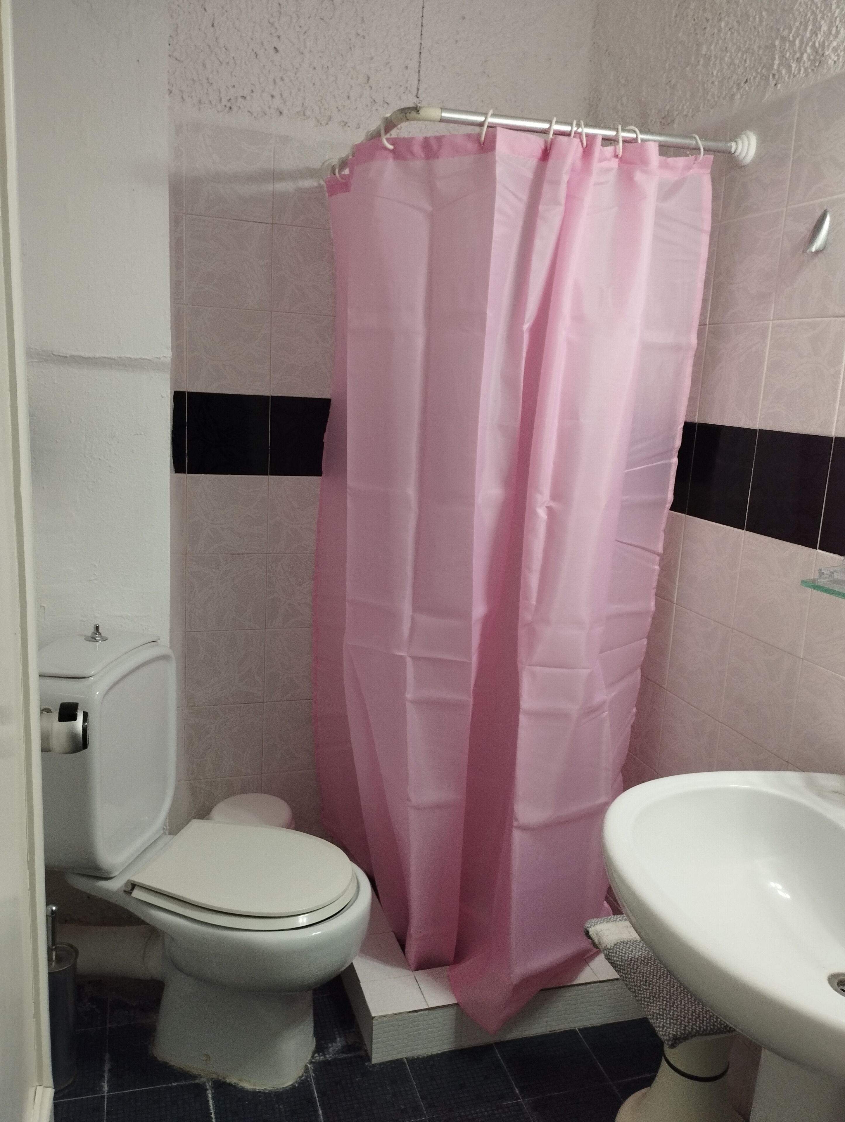 Un baño con inodoro, lavamanos y cortina de ducha rosa.