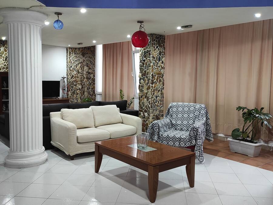 Una sala de estar con un sofá color beige, una mesa de centro de madera, un sillón estampado, una pared de piedra y un colgante de luz rojo.