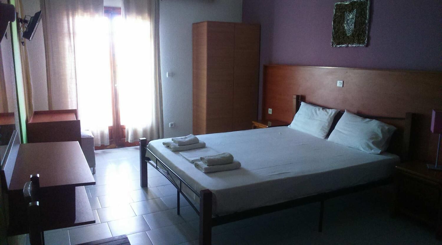 A hotel room with a bed, a desk, a wardrobe, and a window with curtains.
