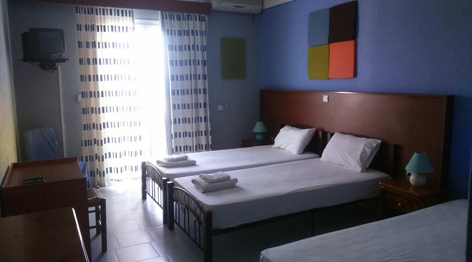 Une chambre d’hôtel avec deux lits, un bureau, une chaise, une télévision et une fenêtre avec des rideaux.