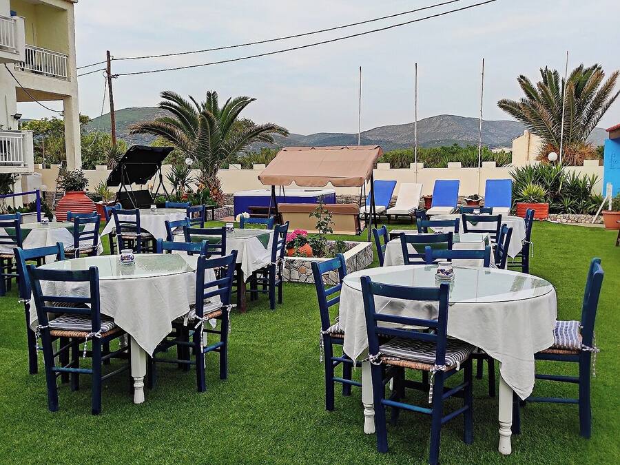 Un espacio de comedor al aire libre con mesas y sillas, rodeado de follaje y vistas a colinas.