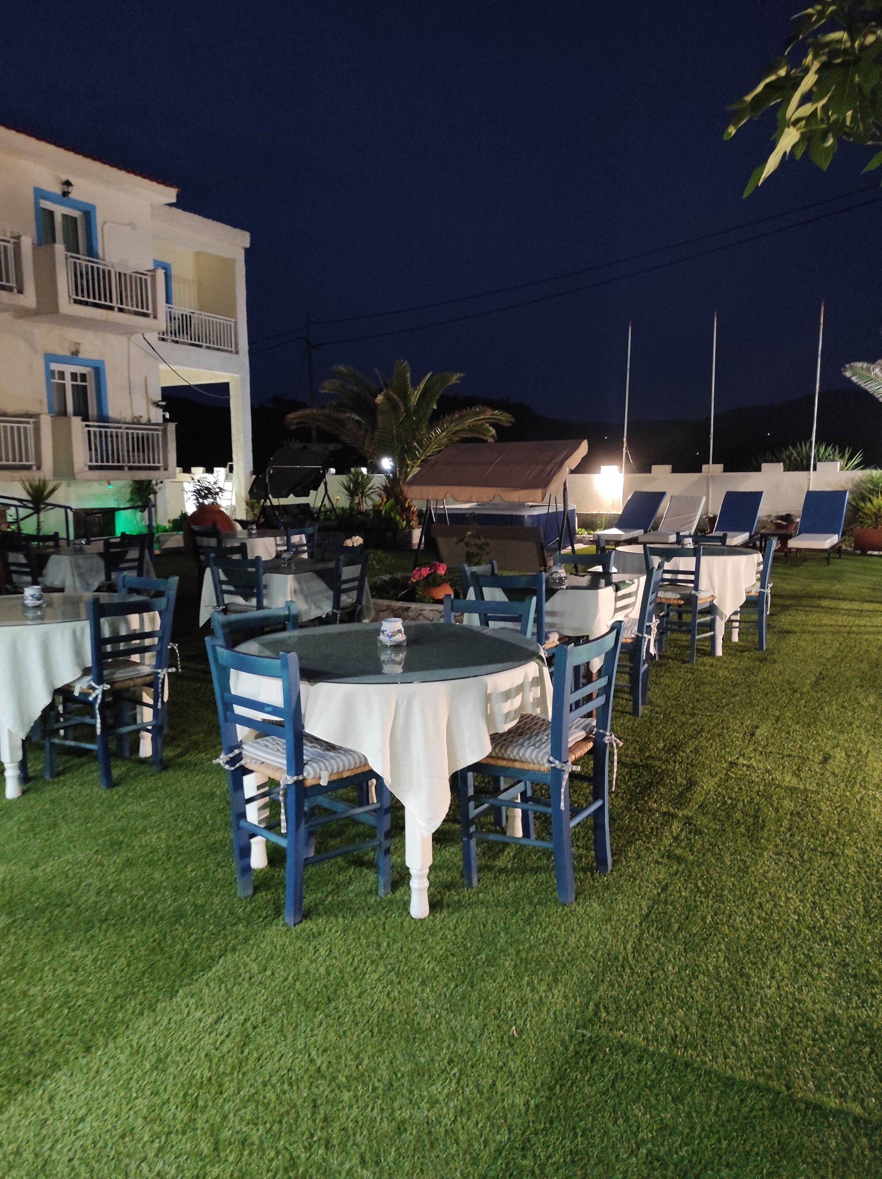 An outdoor dining area with round tables and blue chairs, surrounded by a grassy lawn.