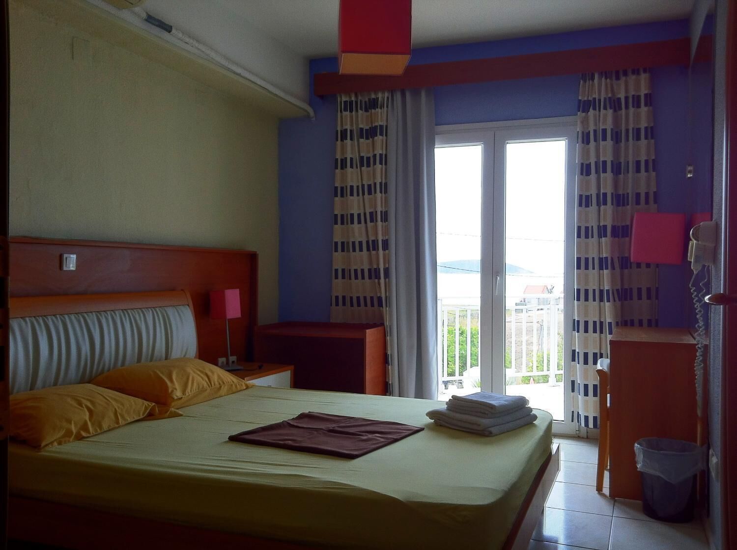 Una habitación de hotel con cama, mesita de noche, escritorio, silla, ventana con cortinas y vistas al exterior.