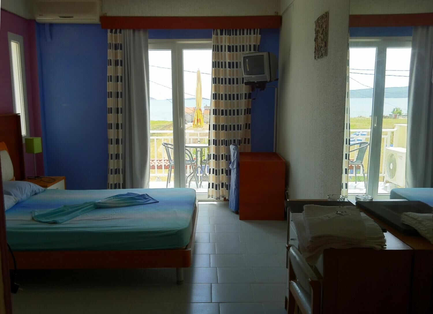 Habitación de hotel con cama, escritorio, silla, televisión y balcón con mesa y sillas.