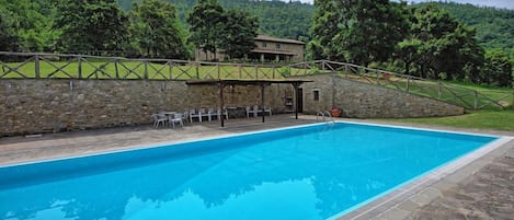 A swimming pool with stone walls and a covered seating area.