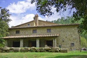 A stone house with a tiled roof, a chimney, and a porch with a table and chairs. - Villa Cretole (Monterchi)