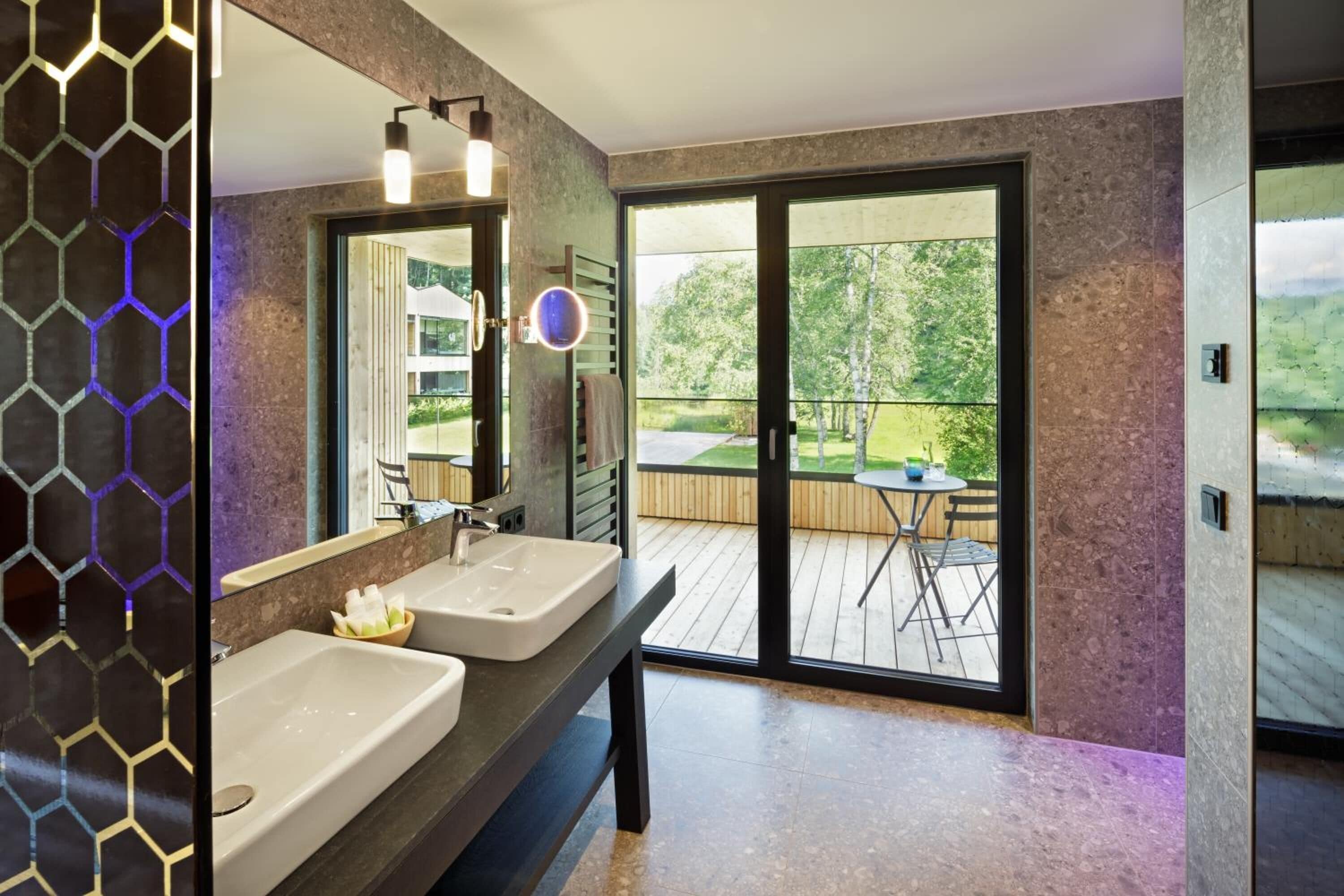 Un baño moderno con dos lavamanos, un espejo grande y vistas a una terraza exterior con mesa y sillas.