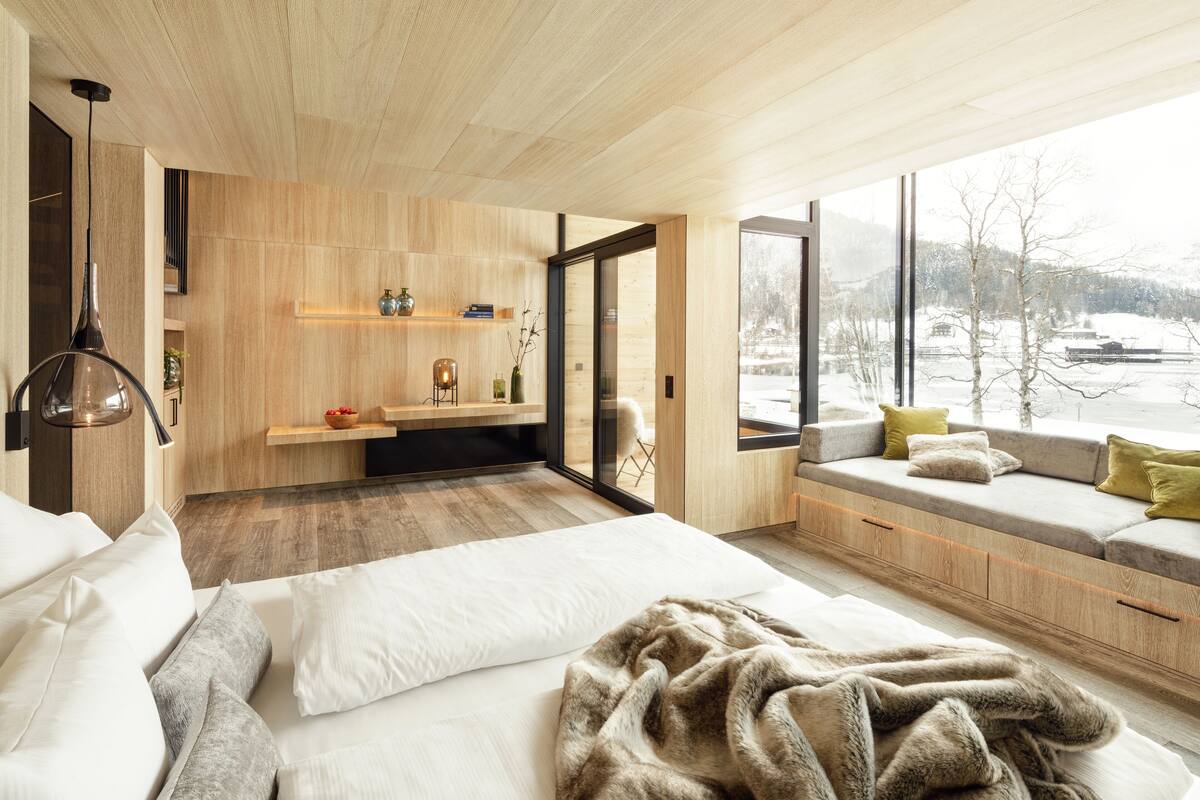 Une chambre moderne avec un grand lit, un coin salon confortable agrémenté de coussins, un mur en bois et une vue sur un paysage enneigé.