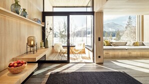 A modern interior with a wooden floor, a black rug, a wooden bench, a glass door leading to a balcony, and a seating area with cushions. - Alpenhotel Kitzbühel (Kitzbuhel)