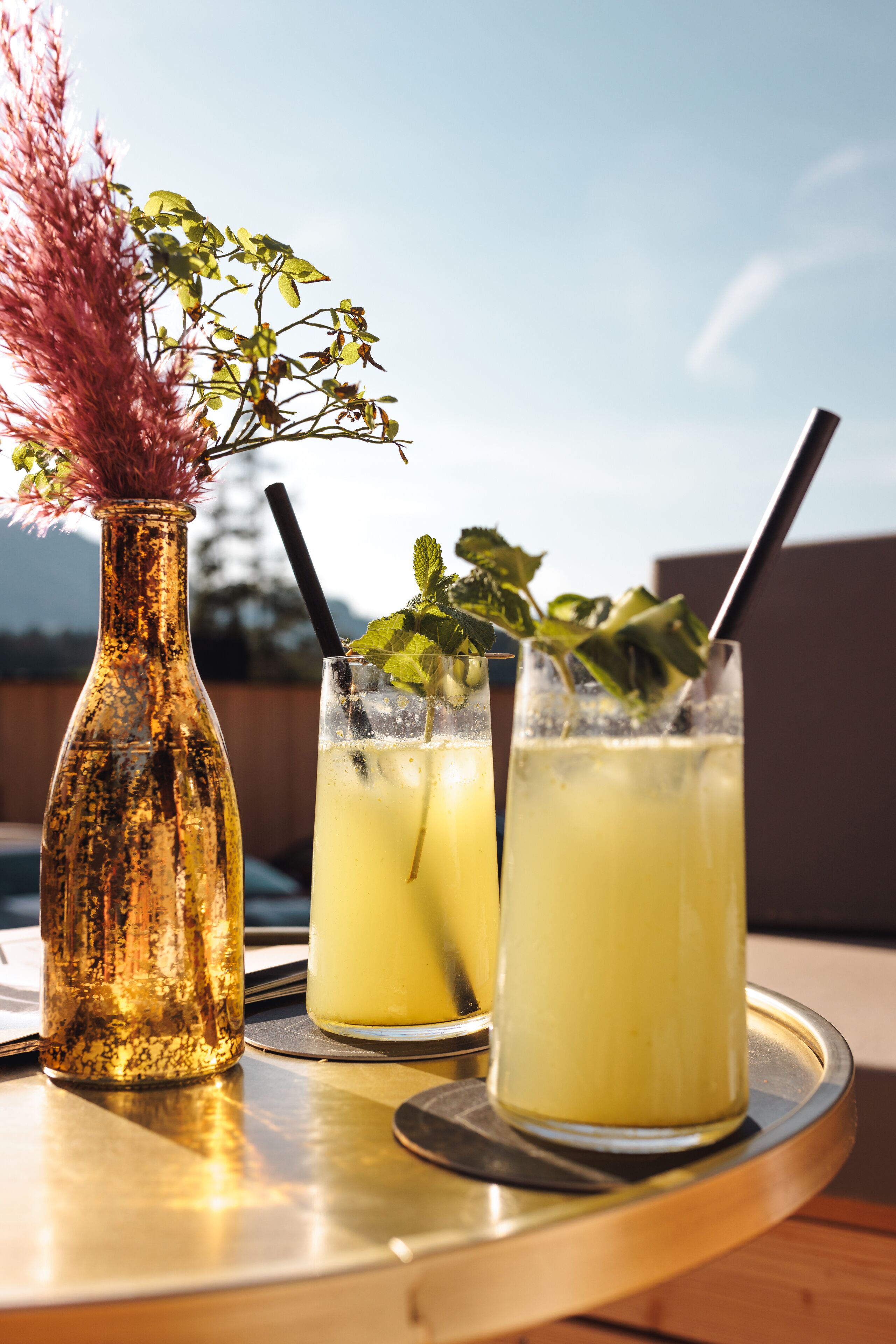 A table with a glass of iced tea, a bottle of water, and a decorative vase with dried flowers.