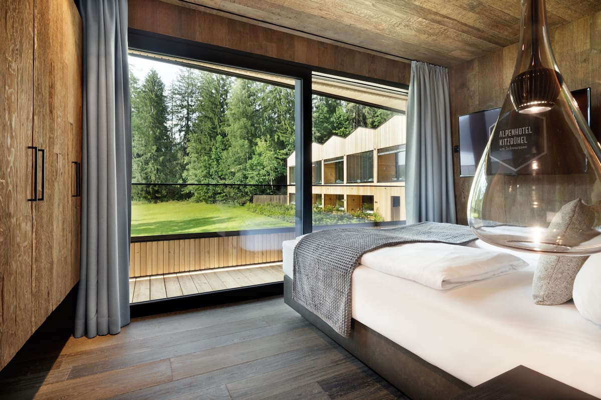 Une chambre d’hôtel moderne dotée d’une grande fenêtre, d’un plancher en bois, d’un lit recouvert d’une couette blanche et d’un téléviseur fixé au mur.