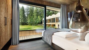 Ein modernes Hotelzimmer mit großem Fenster, Holzboden, einem Bett mit weißer Bettdecke und einem Wand-Fernseher.