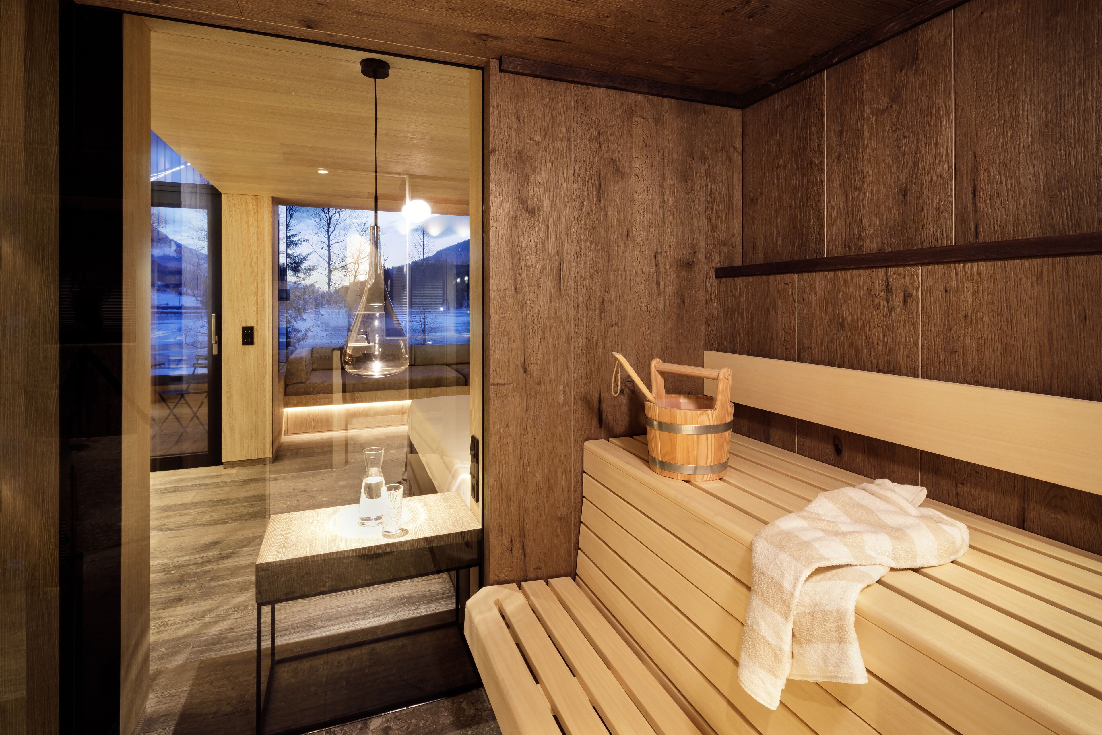 Una sala de sauna con bancos de madera, una mesa con vasos y un cubo de madera.