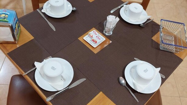 Une table à manger dressée avec de l’assiette, des bols et des couverts blancs, entourée de chaises en bois.