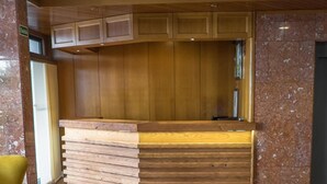 Un hall d’entrée avec un comptoir de réception en bois, un canapé gris agrémenté de coussins jaunes et un fauteuil jaune.