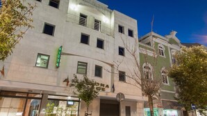 Un hôtel à la façade moderne, doté de nombreuses fenêtres et d’une enseigne verte indiquant la présence d’un restaurant.