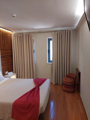 Une chambre d’hôtel avec un grand lit, un petit tabouret, une fenêtre et des rideaux.
