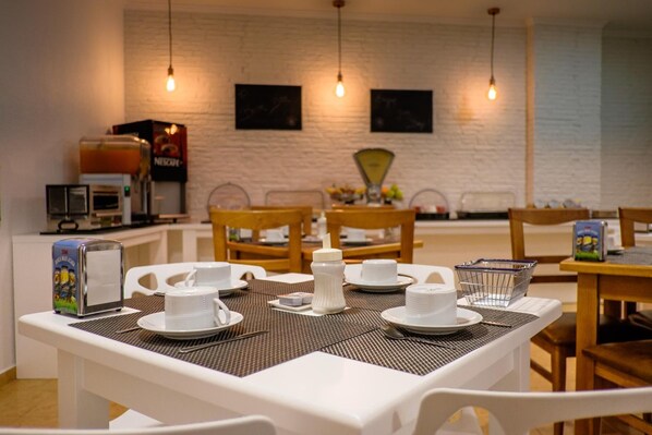 Una mesa de desayuno con vajilla blanca, un dispensador de zumo y una cafetera.