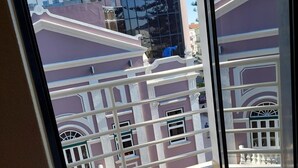 Une vue à travers la fenêtre d’un bâtiment doté d’un balcon, avec un sol carrelé et une balustrade blanche.
