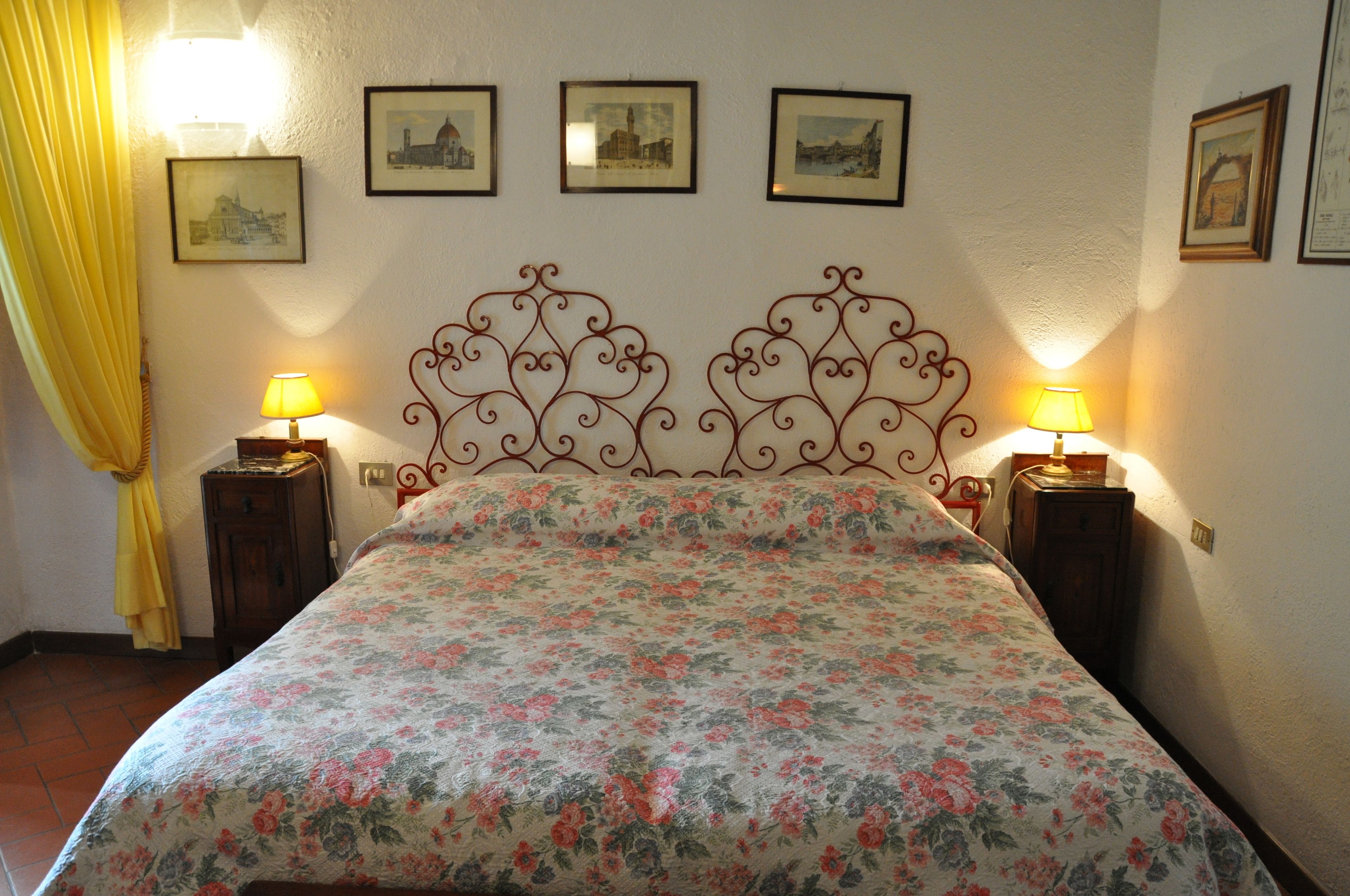 A bed with a floral bedspread, two bedside tables with lamps, and framed pictures on the wall.