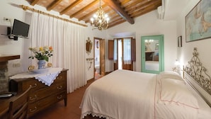 Un dormitorio con cama, cómoda de madera y televisor sobre una repisa.