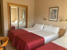 A hotel room with two single beds, a wooden wardrobe, a mirror, and a framed picture on the wall.
