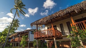 Ein Resort mit strohgedeckten Häusern, Holzbalkonen und üppiger Vegetation.