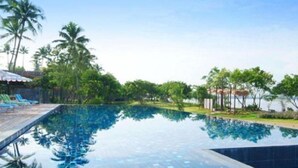 Ein Swimmingpool mit klarem, blauem Wasser, umgeben von Palmen und einer gefliesten Liegefläche.