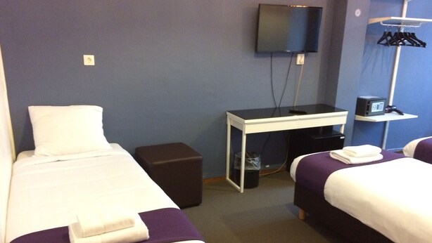 A hotel room with two beds, a desk, a TV, and a wardrobe. - Hotel Bellington (Amsterdam)