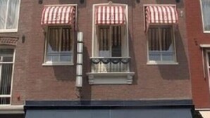 A multi-story building with six windows, each with a red and white striped awning. - Hotel Bellington (Amsterdam)