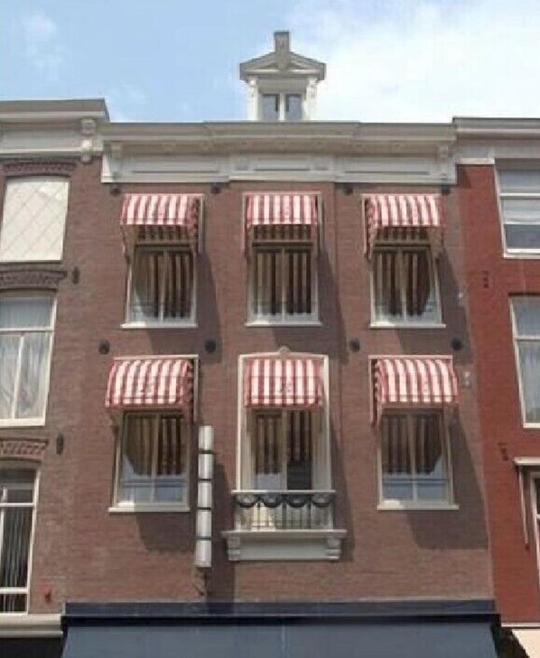 A multi-story building with six windows, each with a red and white striped awning. - Hotel Bellington (Amsterdam)