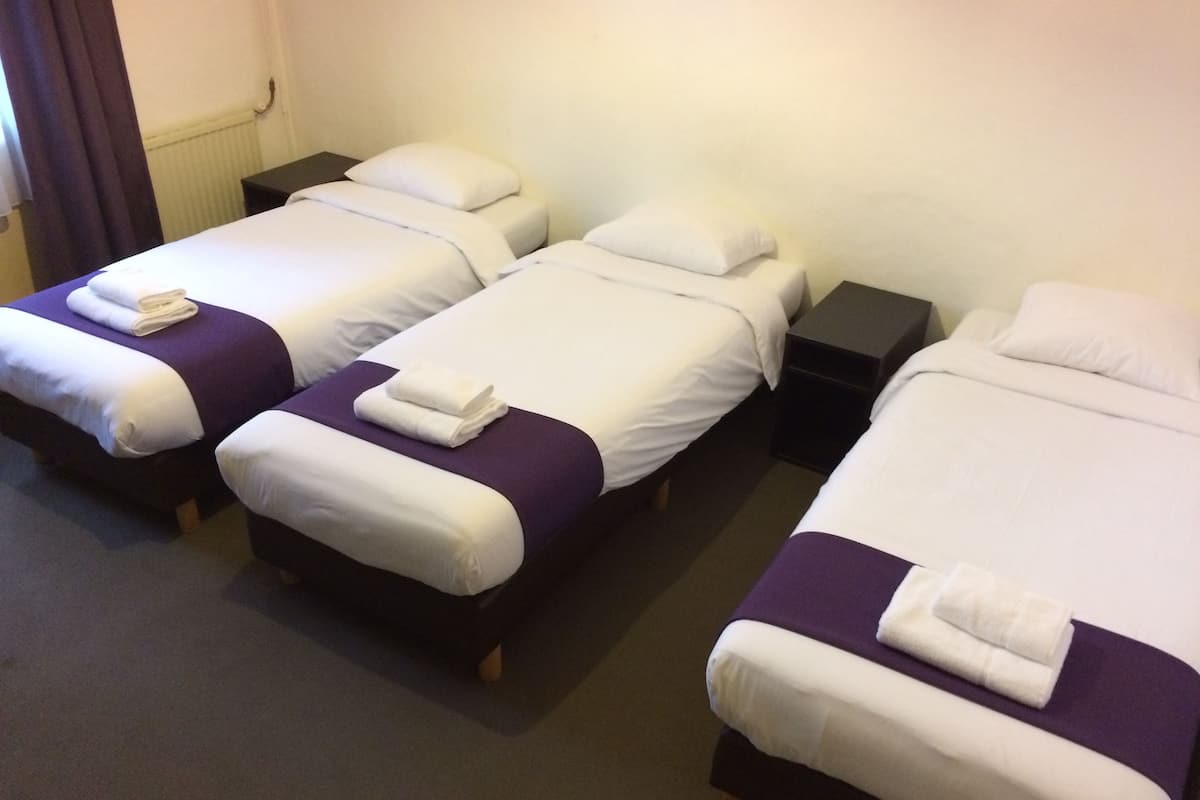 A hotel room with three single beds, each with white linens and purple bedspreads.