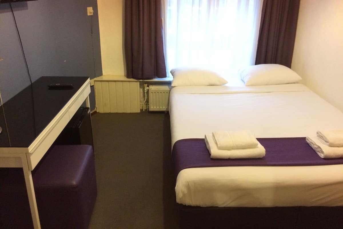 A hotel room with a bed, a desk, and a window with curtains.