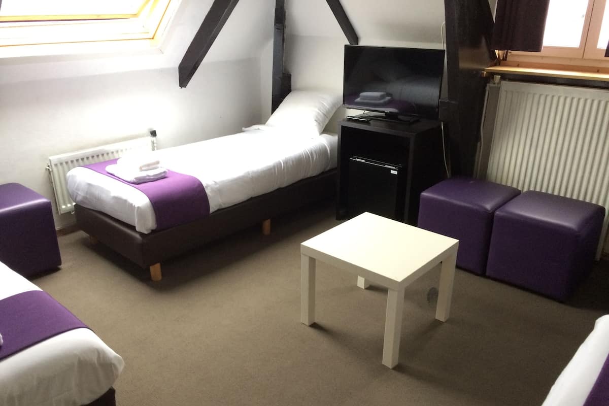 A small, well-lit room with a bed, a sofa, a table, and a TV.