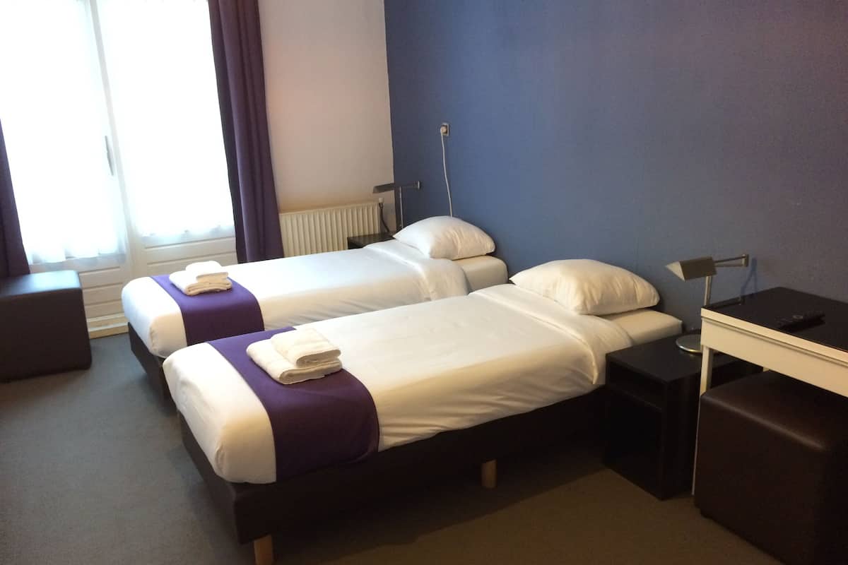 A hotel room with two single beds, a desk, and a chair.
