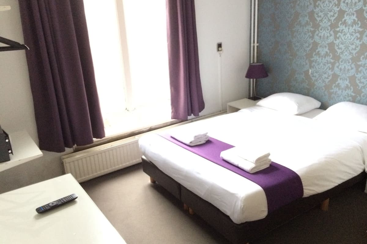 A hotel room with a bed, a bedside table, a lamp, and a window with curtains.