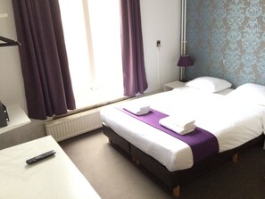 A hotel room with a bed, a bedside table, a lamp, and a window with curtains. - Hotel Bellington (Amsterdam)