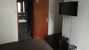 A room with a wooden door, a television mounted on the wall, and a small black speaker. - Hotel Bellington (Amsterdam)