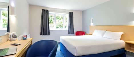 A hotel room with a bed, a desk with a chair, a telephone, and a window with curtains.