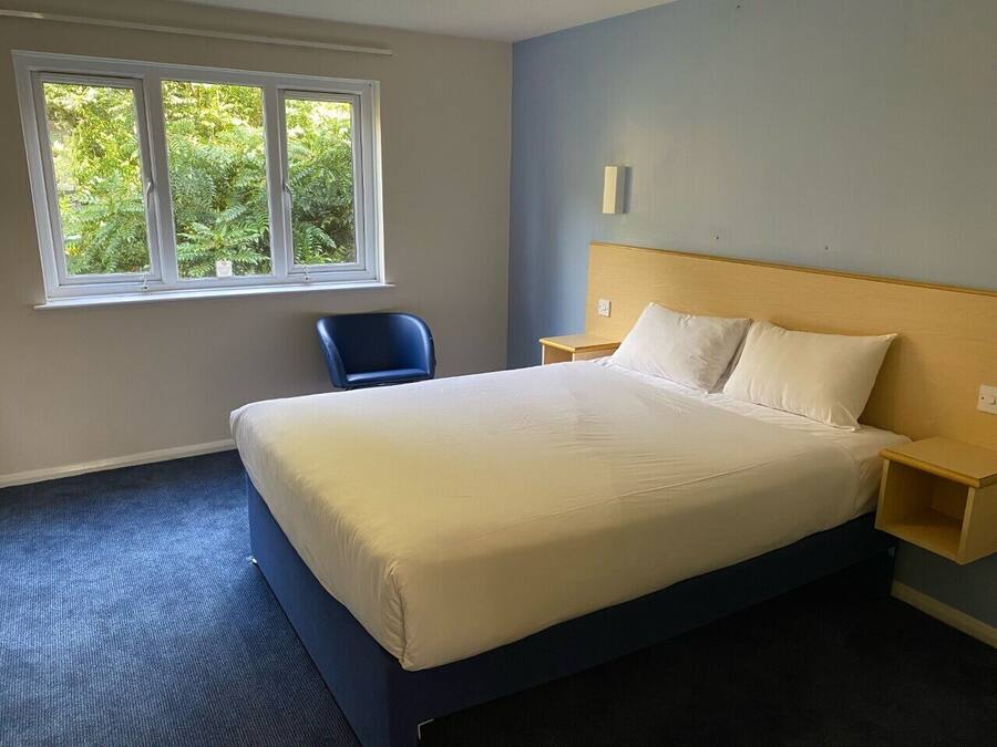 Un dormitorio con cama, una silla, una ventana y una mesita de noche.